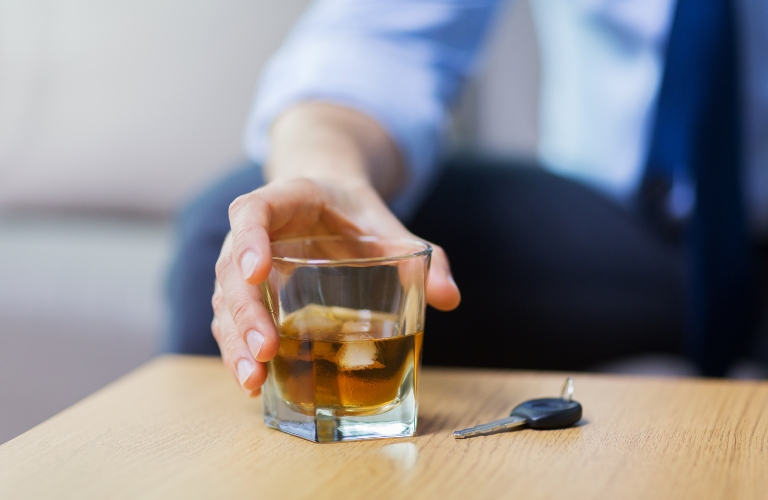 male driver hand with whiskey glass and car key on table